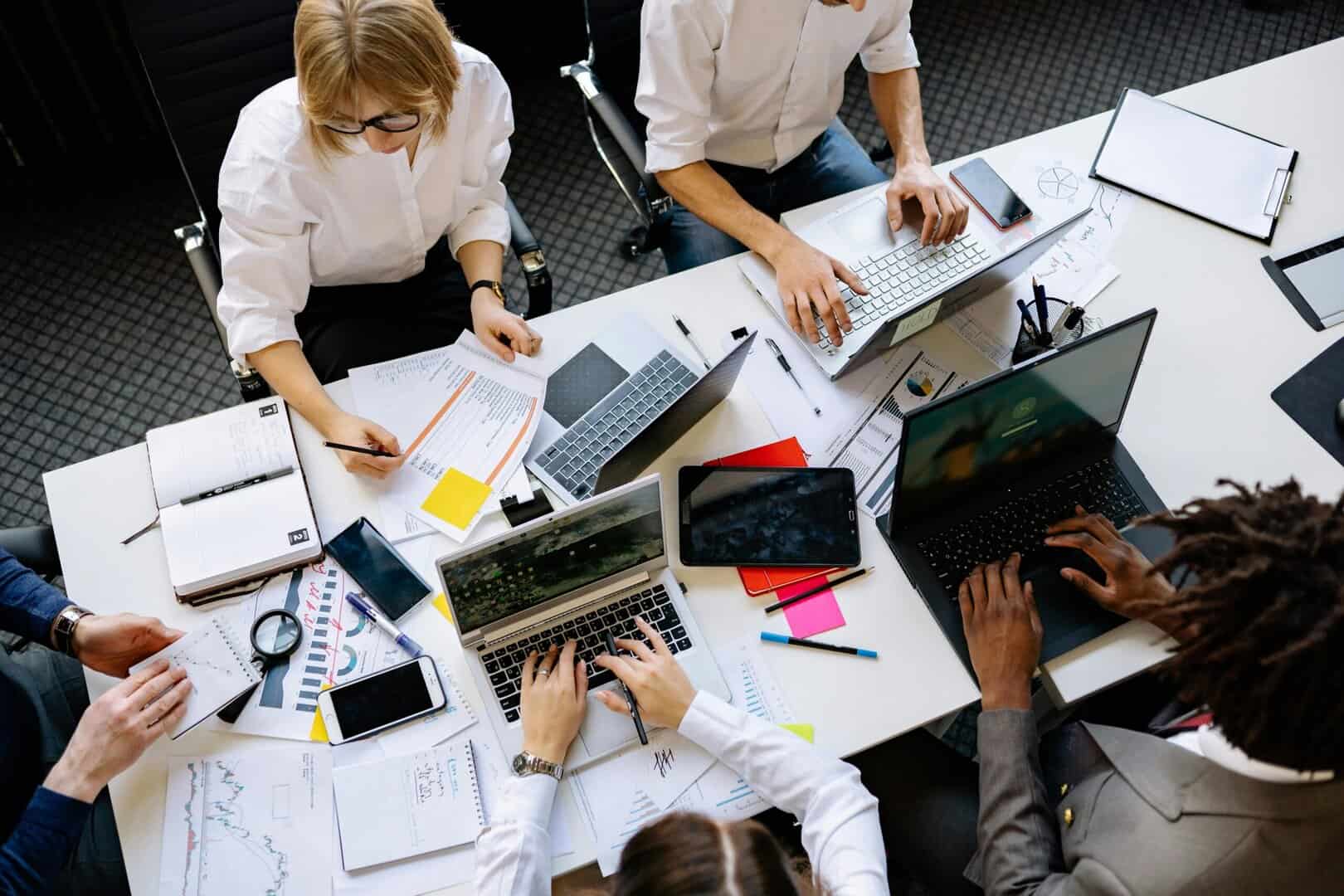 Vibrant office teamwork scene with laptops, documents, and diverse professionals in a meeting.